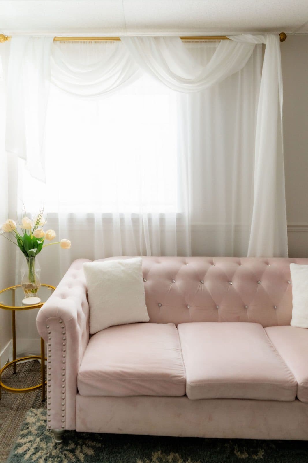 A therapy room with a blush pink tufted sofa, sheer curtains, and fresh tulips