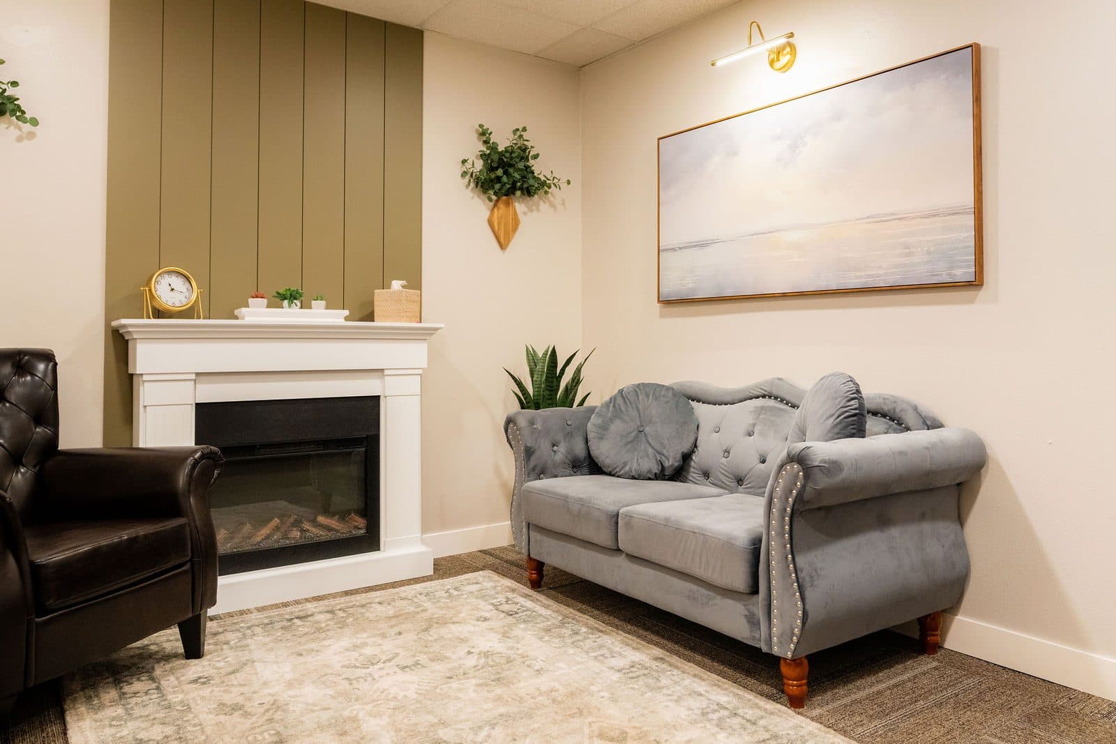 A cozy office with a fireplace, a gray loveseat, and a leather armchair