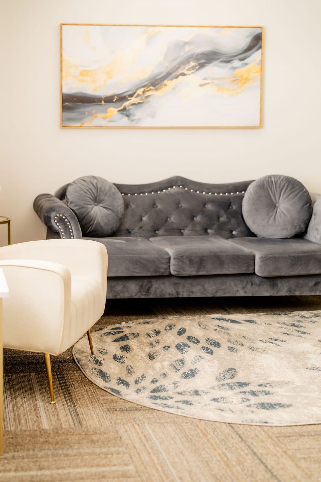 A therapy room with a gray velvet sofa, a cream armchair, and soft natural light