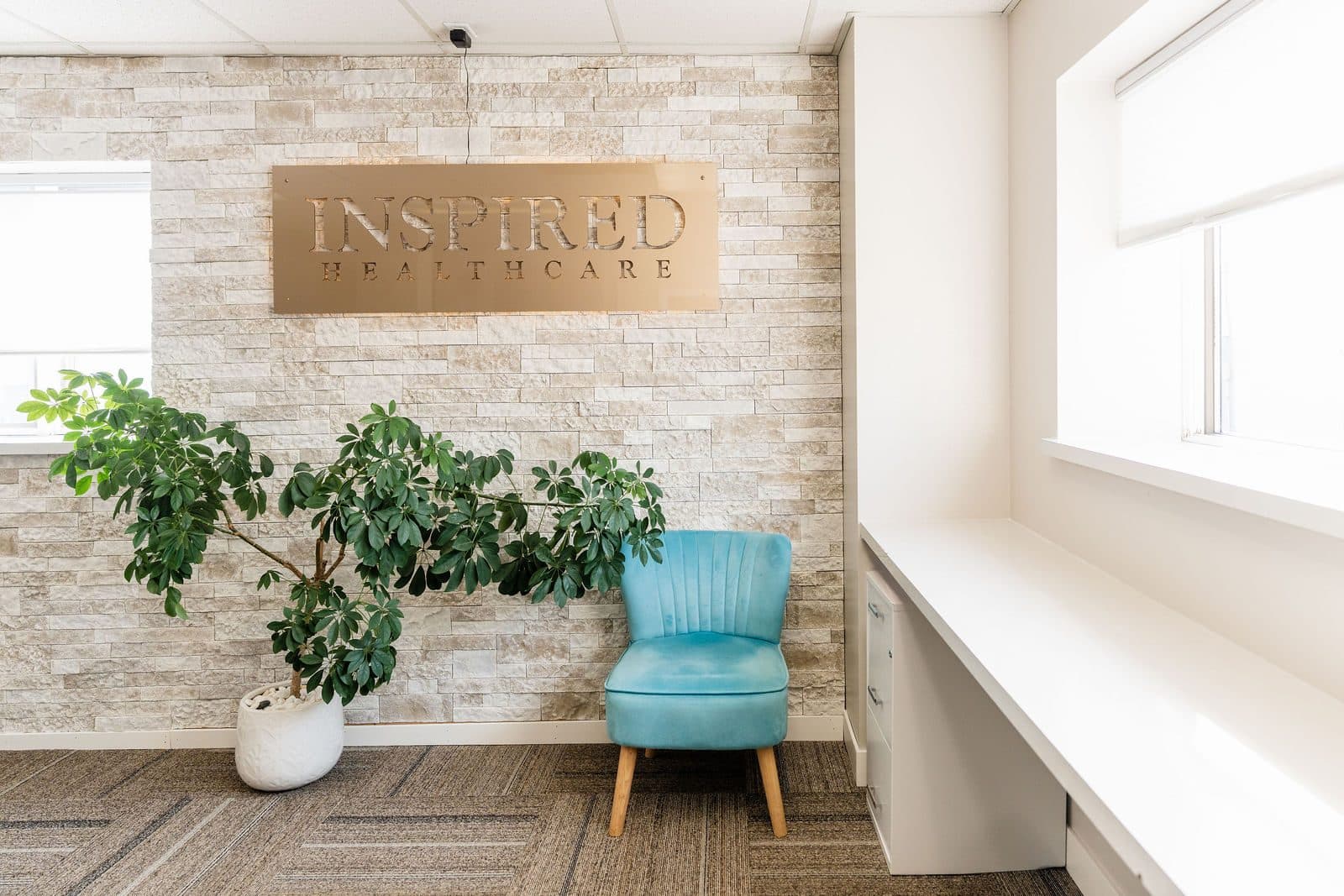 The Inspired Healthcare lobby: a stone wall with the Inspired Healthcare sign, green plants, and a teal chair