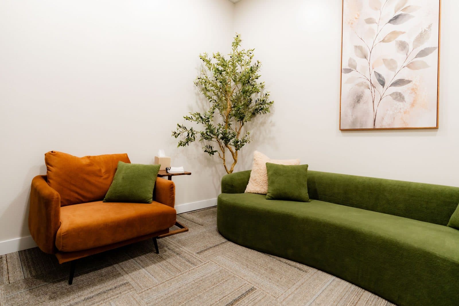 An office with a green sofa, a rust armchair, and a small olive tree